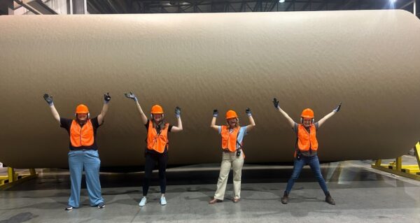 Women in Manufacturing Tennessee members wearing safety gear beside a large paper roll at Domtar Kingsport.